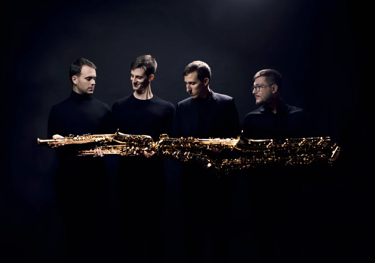 Porträt des Kebyart Saxophonquartetts: Vier Musiker in schwarzer Kleidung präsentieren ihre goldenen Saxophone vor dunklem Hintergrund.